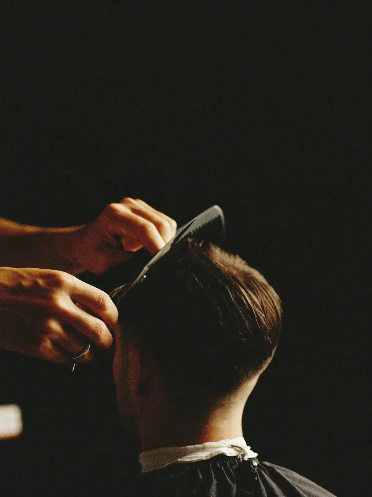 Barbier knipt de nek van een klant bij met schaar en kam in warm zijlicht