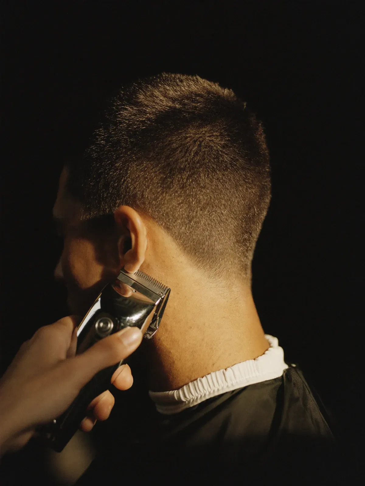 Tondeuse trekt een strakke skin fade in het haar van een klant, gezien van achteren